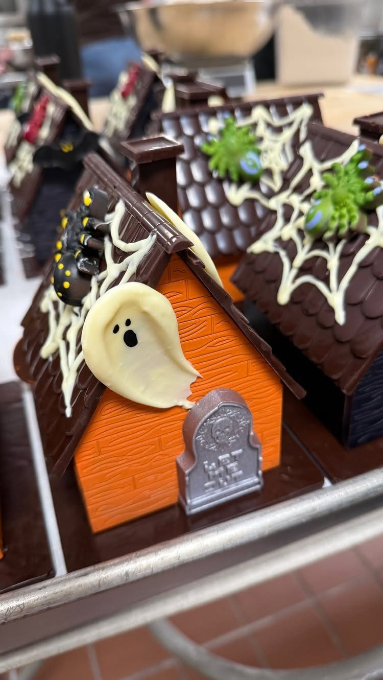 Edible chocolate haunted houses decorated with ghosts, spiders, and white icing spider webs.