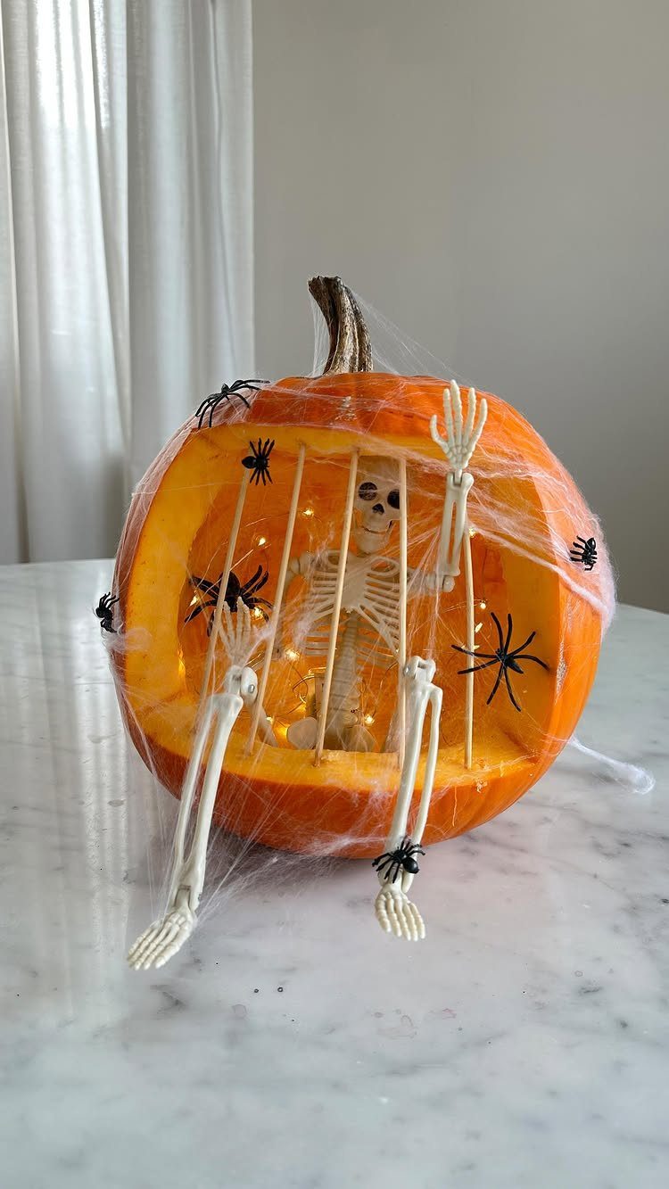 Carved orange pumpkin cage with a small skeleton and spider web decorations