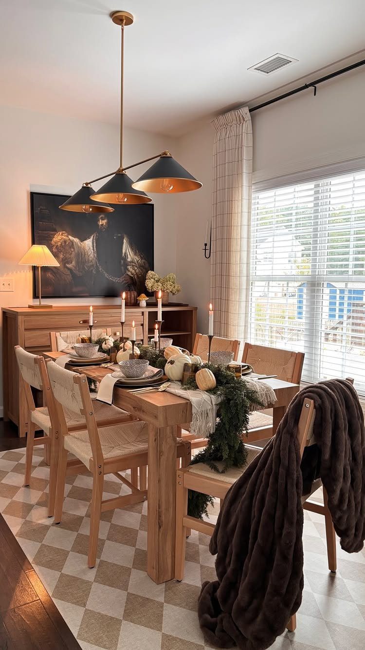 Wooden dining table styled with a long greenery centerpiece, white pumpkins, and layered place settings.