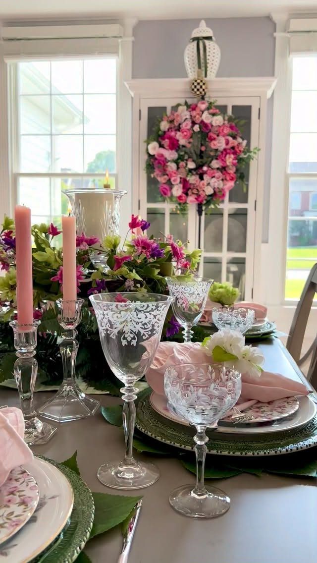 Dining table set with etched crystal glasses, pink candles, and floral centerpieces.