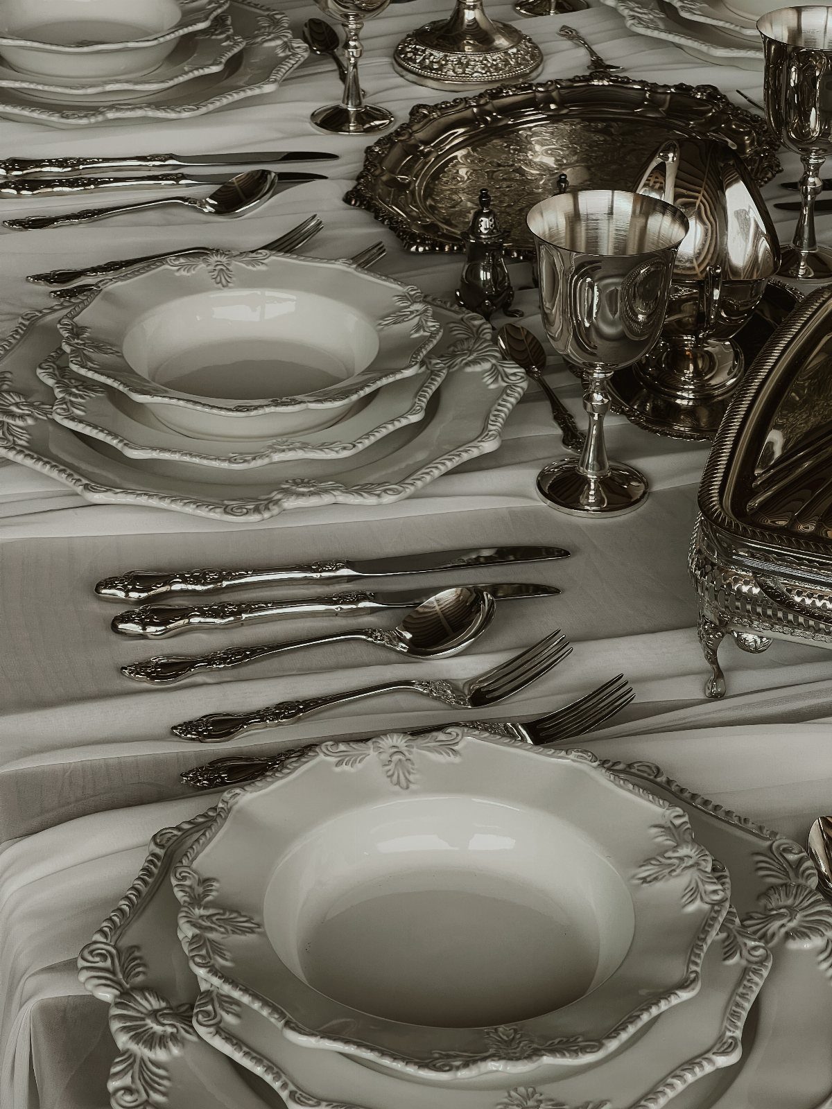 Formal dining table setting with ornate white plates and polished silver tableware.