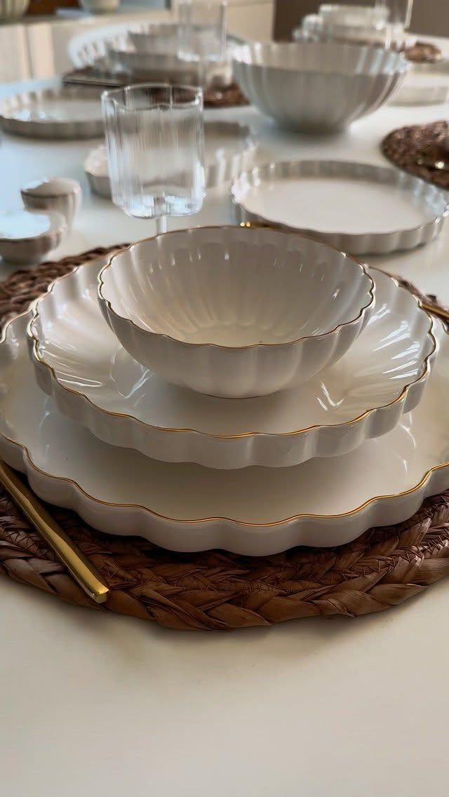 Stacked white scalloped plates and bowl on a brown woven charger plate.