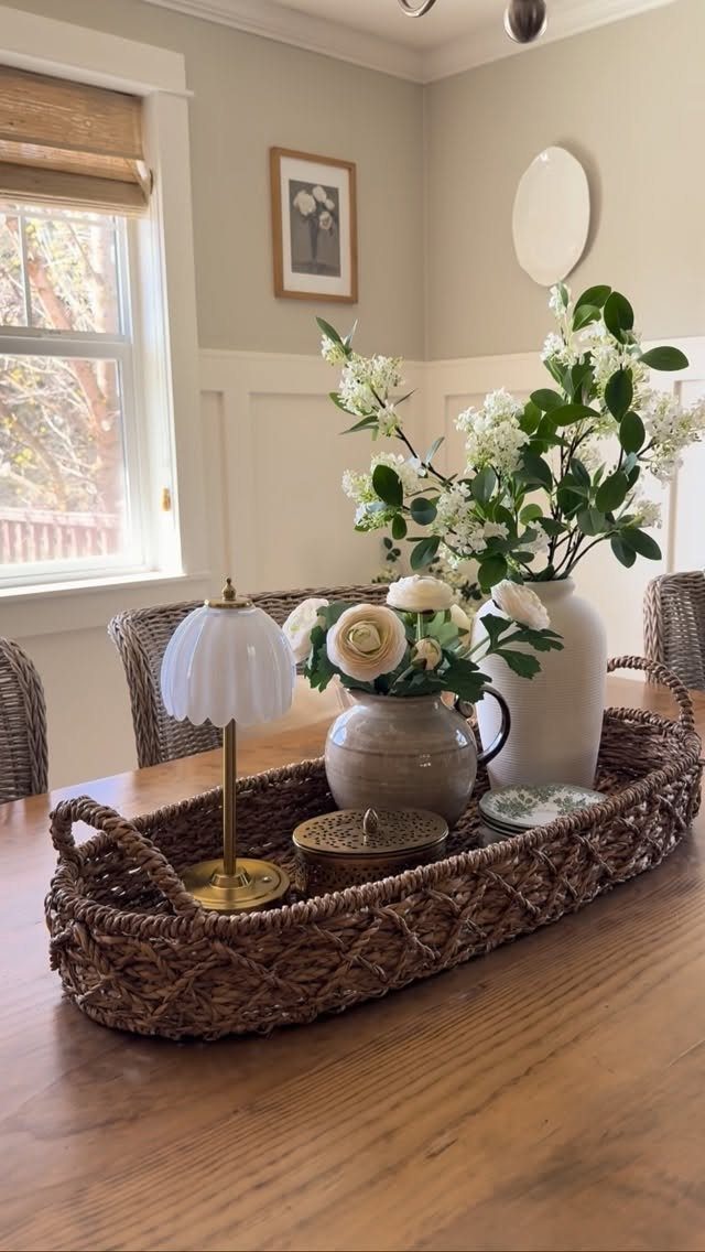 Woven wicker tray centerpiece with white flowers and a small lamp on wooden table