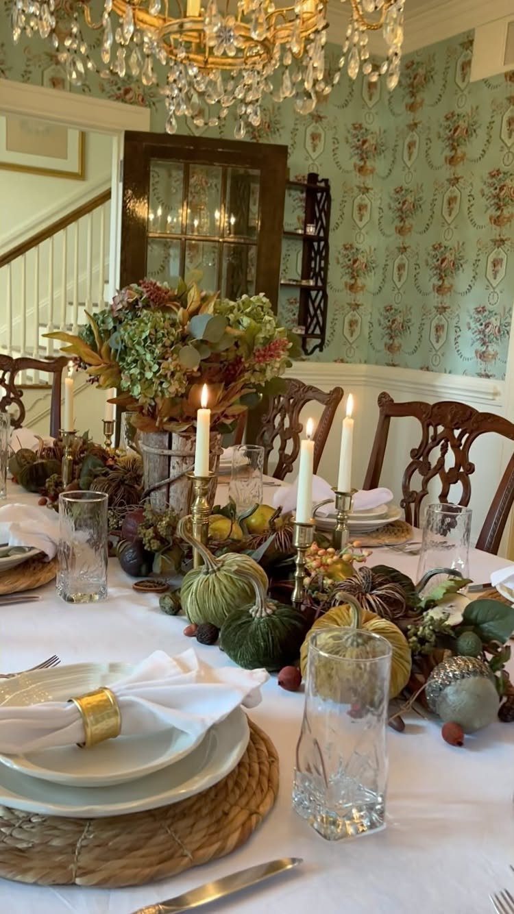 Dining table styled with woven chargers, white linens, pumpkins, and autumn foliage centerpiece.