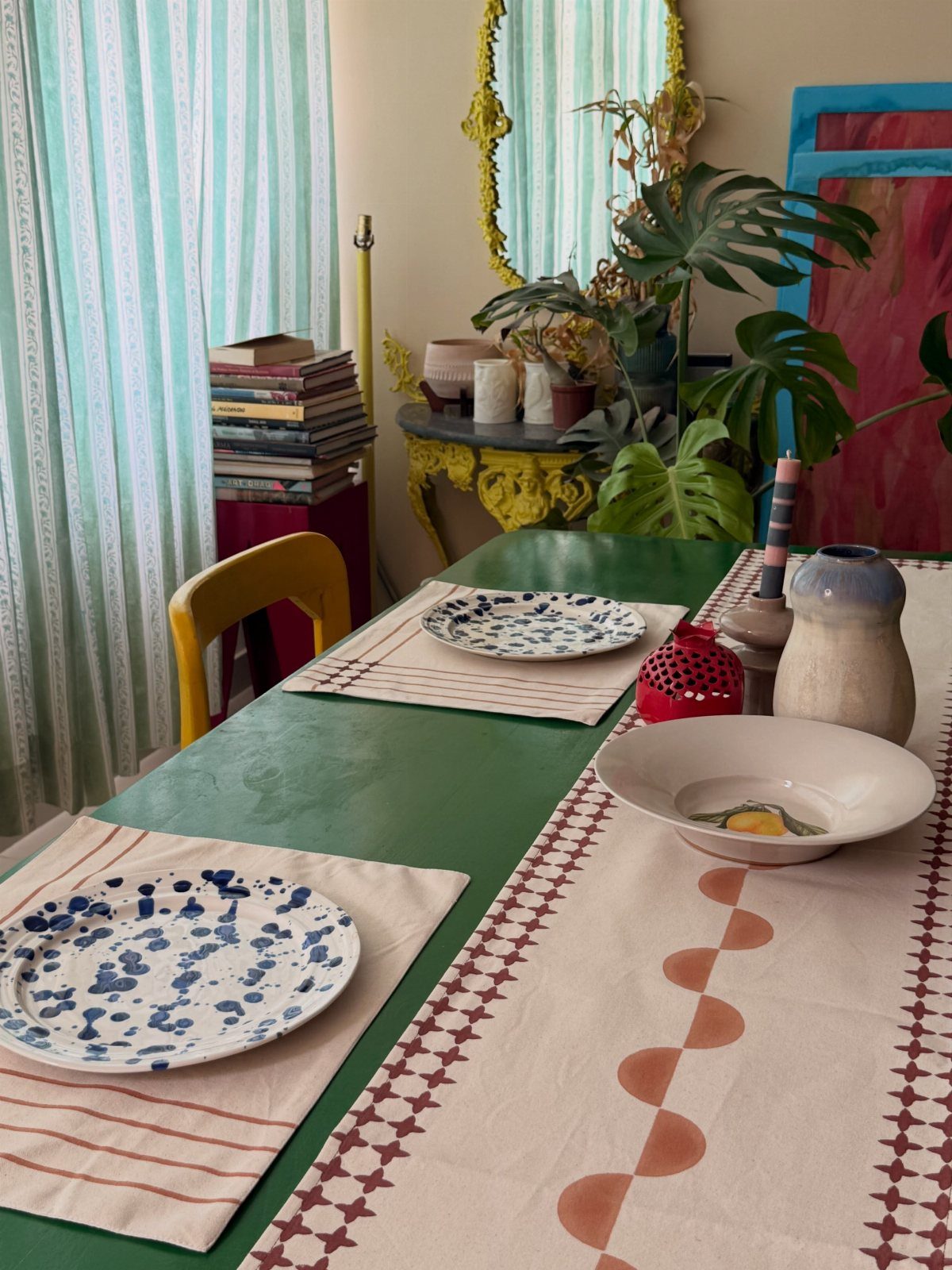 Green dining table styled with mixed patterned tableware, a runner, and speckled plates.