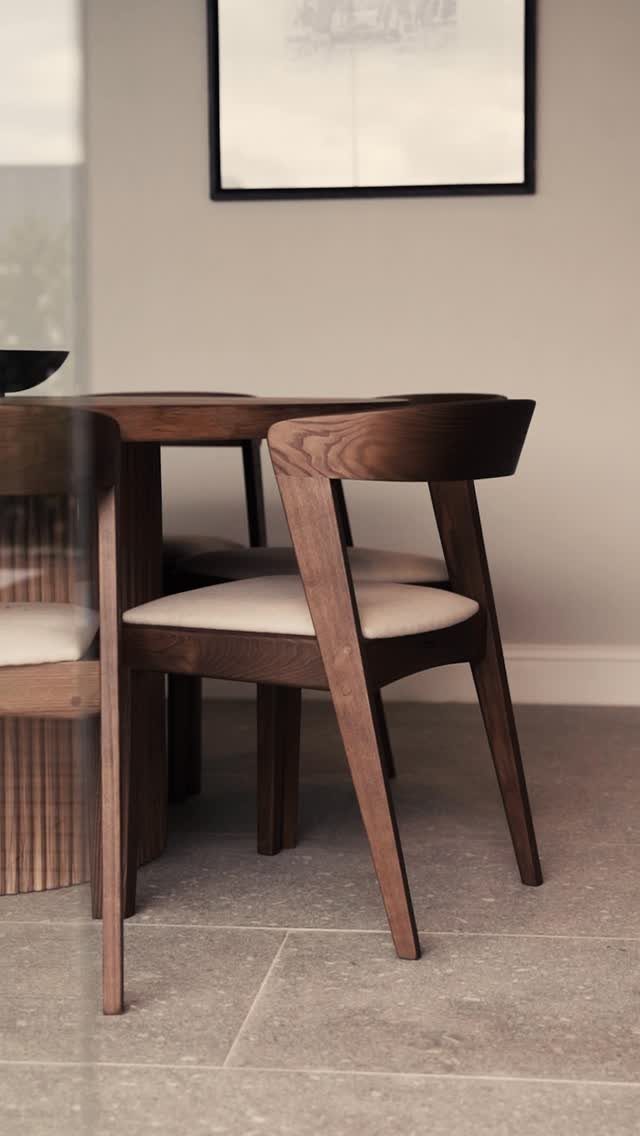 Dark wood dining table and matching chairs with cream cushions on grey tiles.
