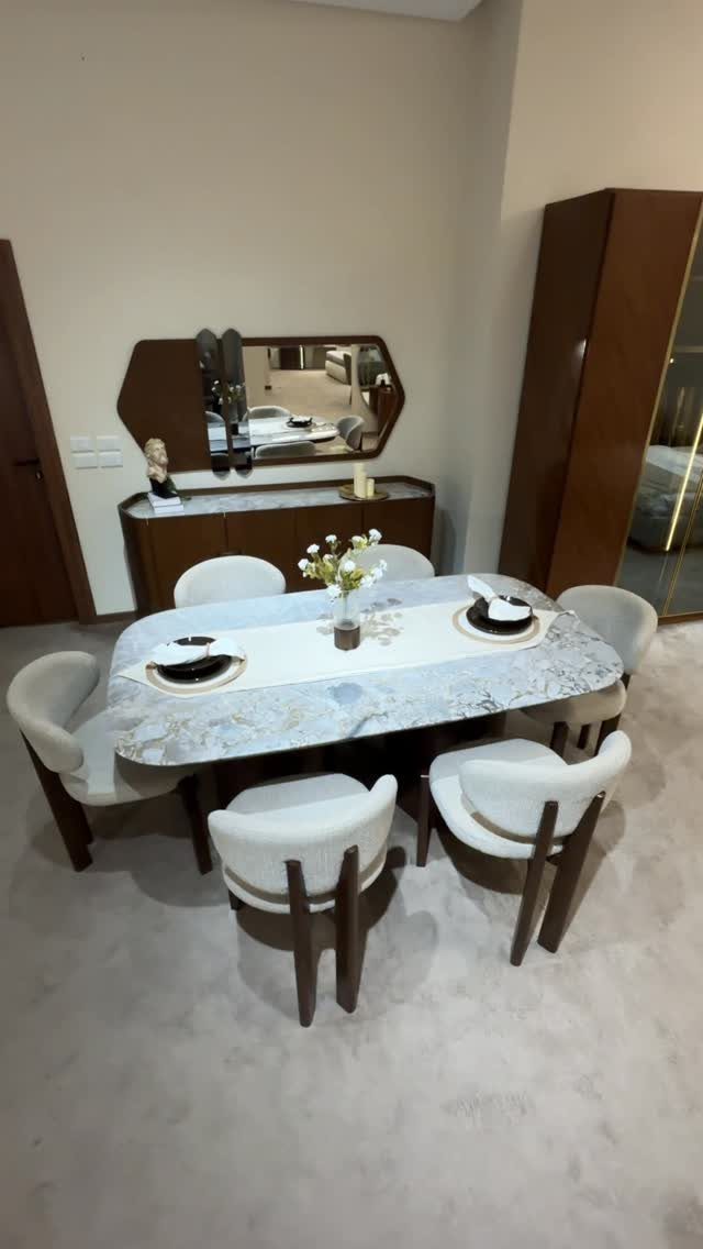 Oval marble dining table with blue veining and white upholstered chairs in a room.