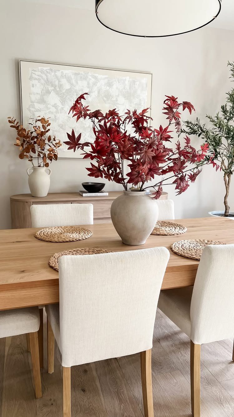 Wooden dining table with white chairs and a vase of red autumn leaves