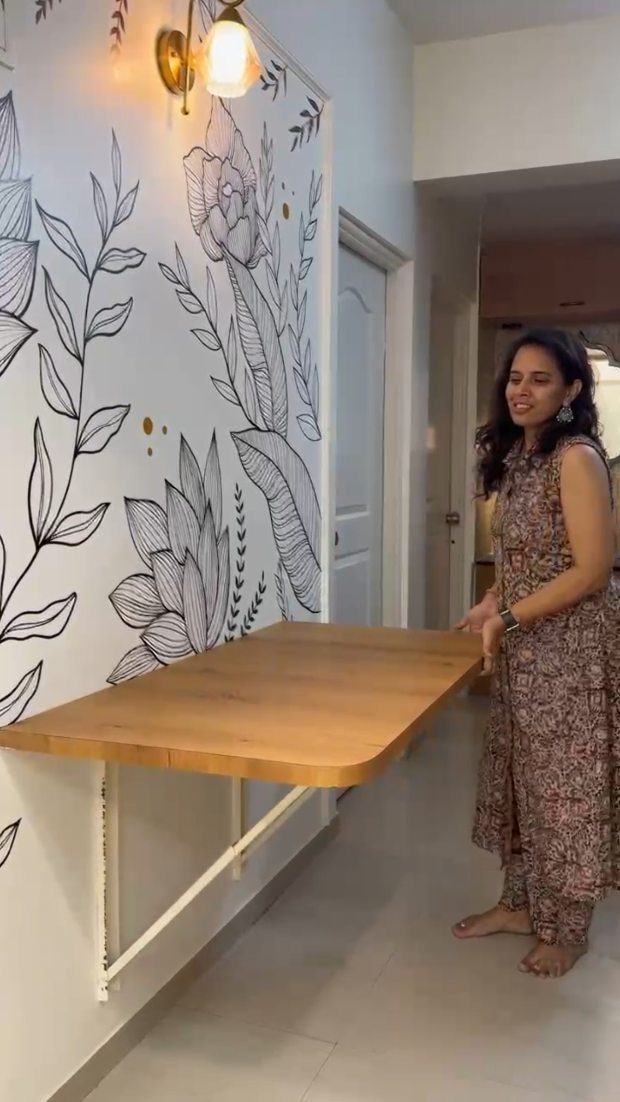 Woman standing by a foldable wooden wall table with floral wall art.