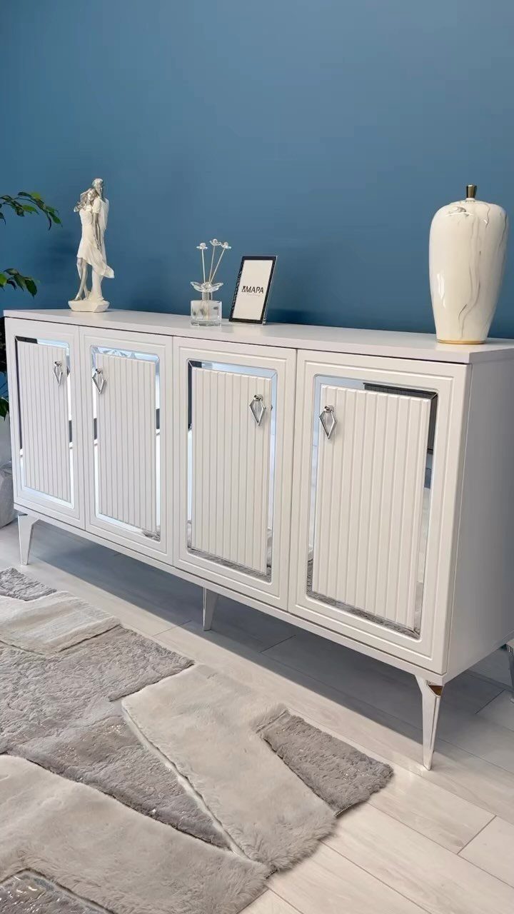 White fluted sideboard with decorative objects against a blue wall and grey rug.