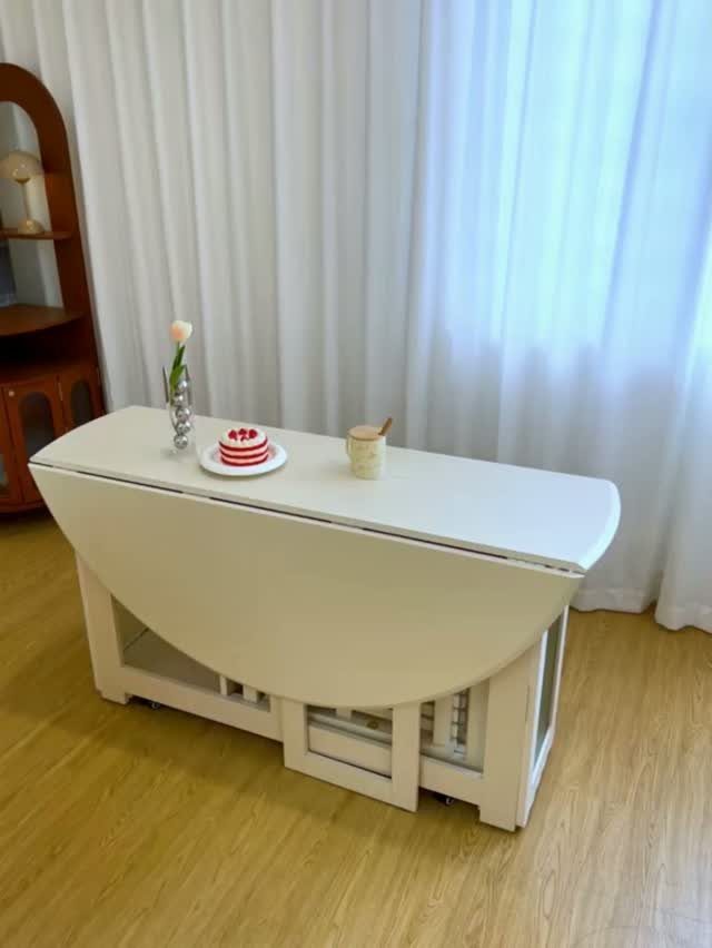 White drop-leaf dining table with a small cake and flower against white curtains.