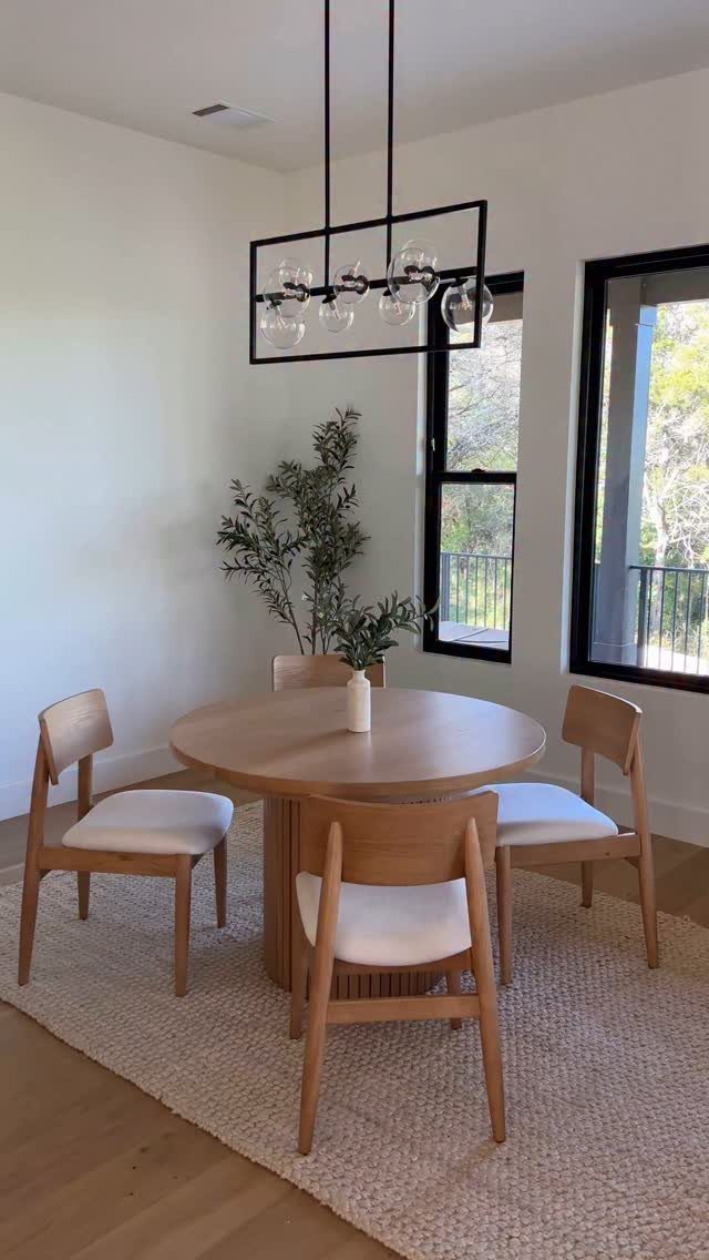 Round wooden dining table with four chairs and a black rectangular chandelier above.