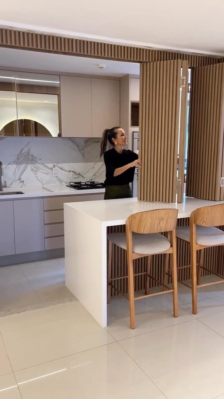 Woman standing by a vertical wooden slat room divider in a modern kitchen.