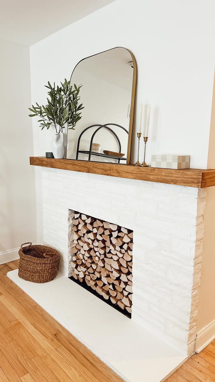 White brick fireplace with a wooden mantel decorated with a mirror and plant.