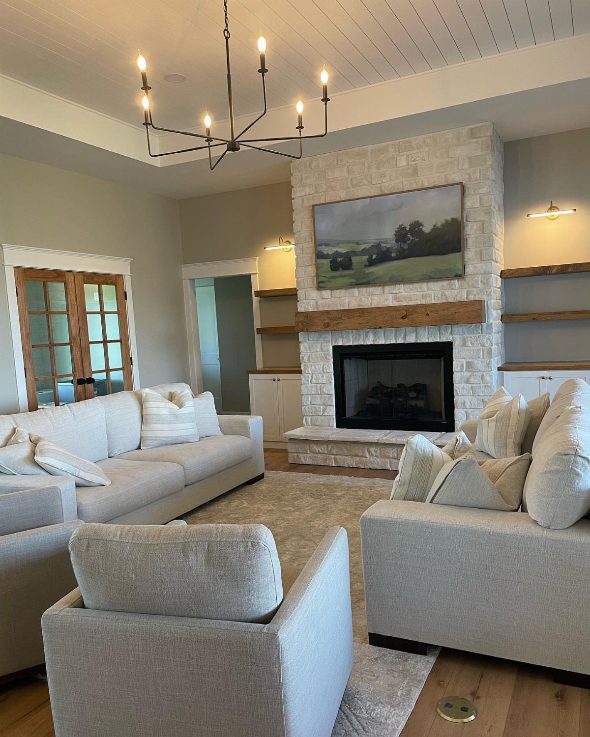 White stone fireplace with wooden mantel and floating shelves in a modern living room