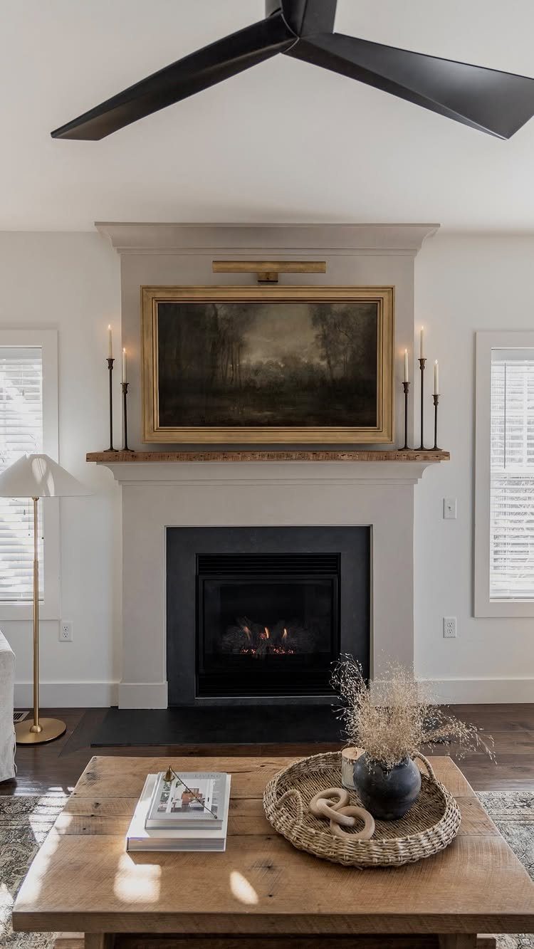 Fireplace mantel decorated with a gold-framed painting and black taper candles in a living room.