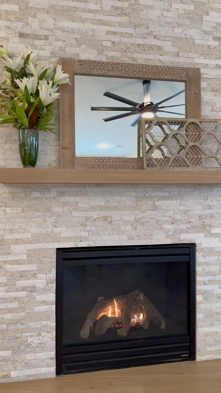 Decorated fireplace mantel with white lilies, a wooden mirror, and geometric decor.