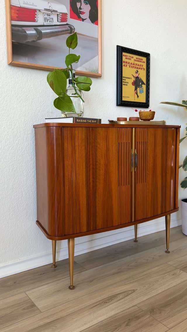 Wooden mid-century modern sideboard with brass legs and handles against a white wall.