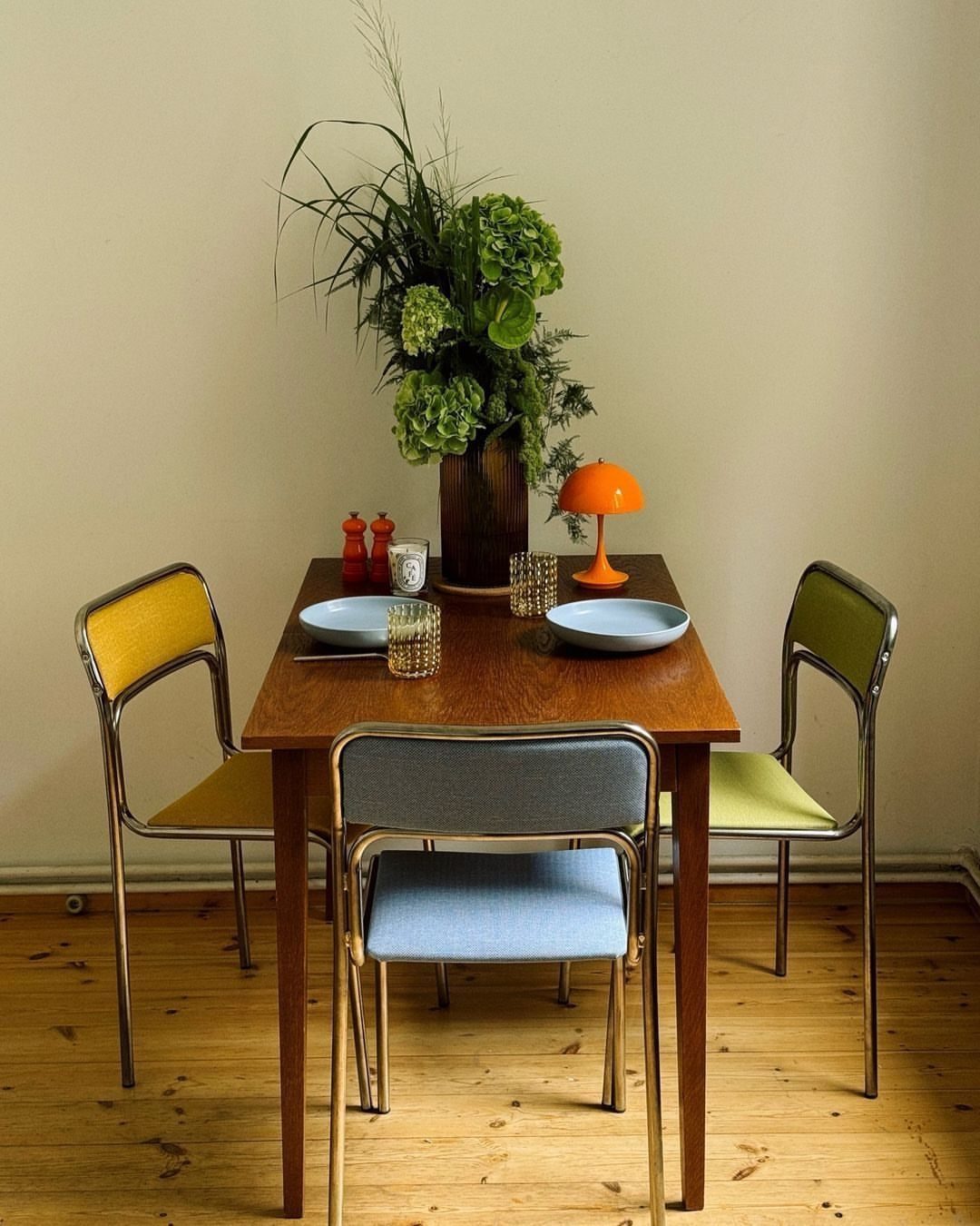 Mismatched yellow, blue, and green mid-century modern chairs around a wooden dining table.