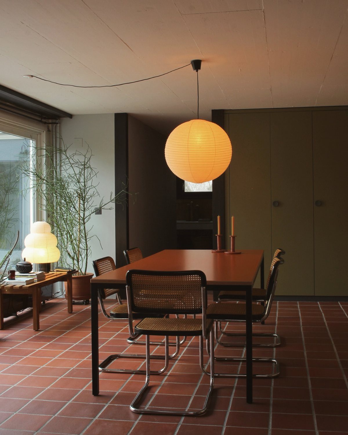 Wooden dining table with cane chairs and a large spherical paper pendant lamp.