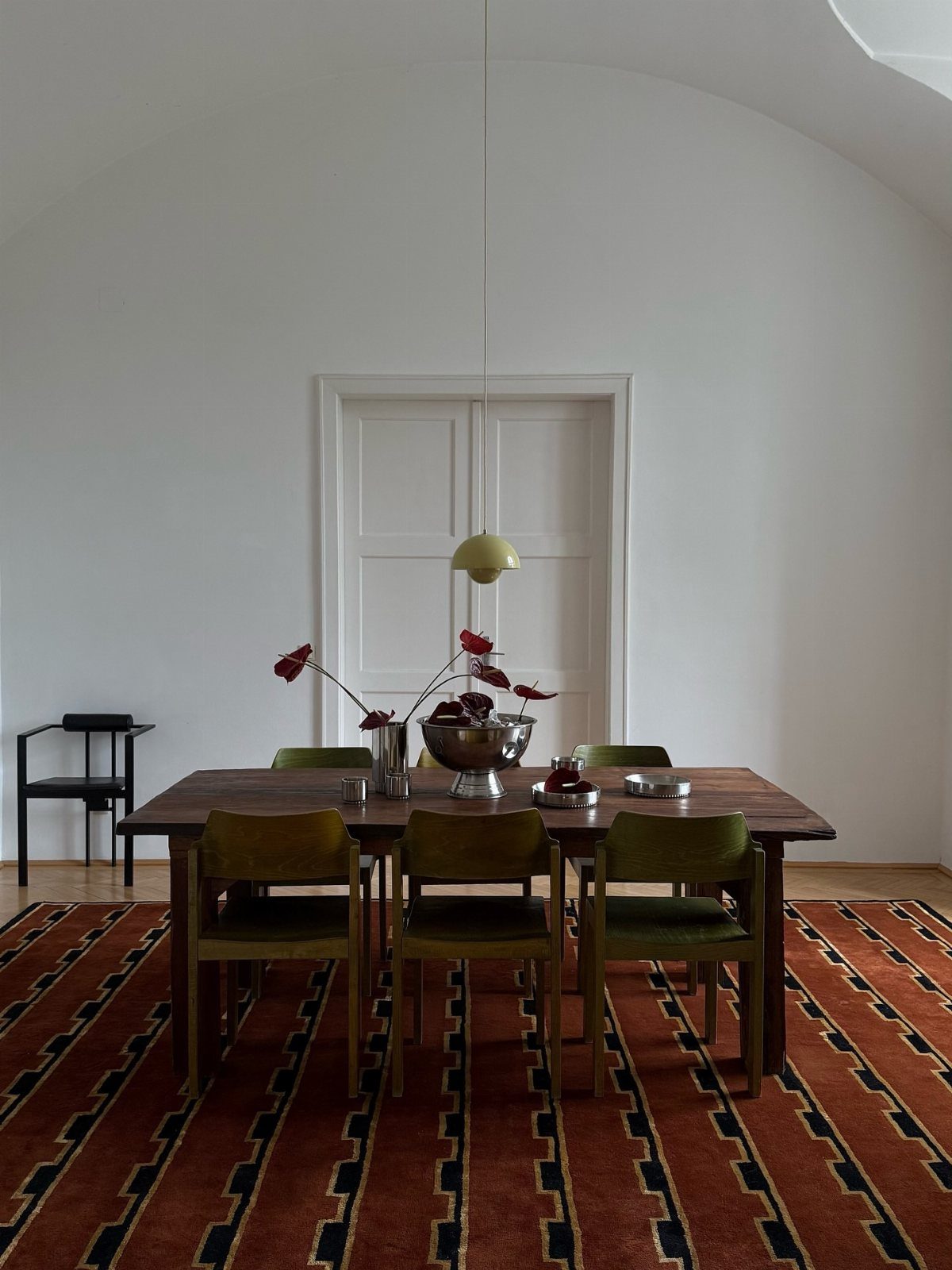 Wooden dining table with green chairs on a red patterned rug in white room