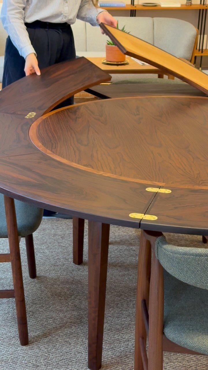 Walnut wood extendable dining table with brass hinges and grey upholstered chairs.