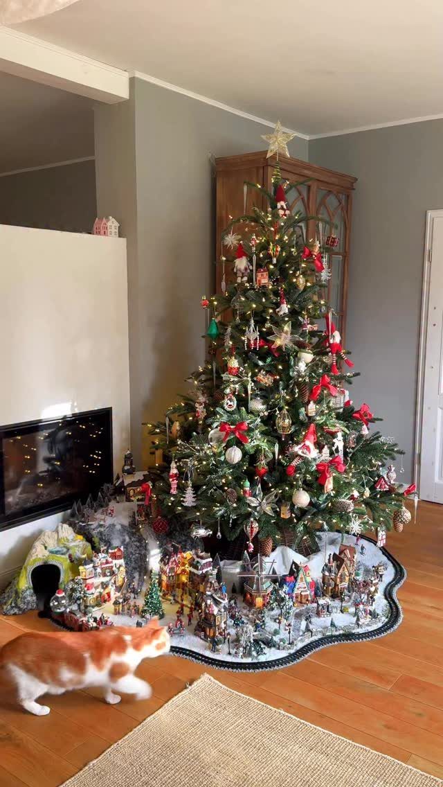 Decorated Christmas tree and miniature village on a wooden floor with a cat.