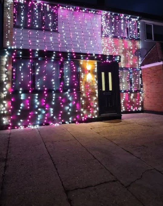 Mobile home exterior decorated with purple and white Christmas lights at night.