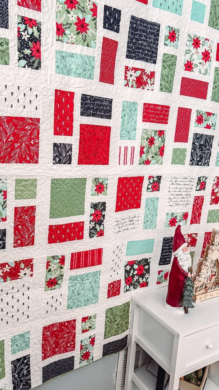 Holiday quilt with red and green patchwork patterns hanging near a Santa figurine.