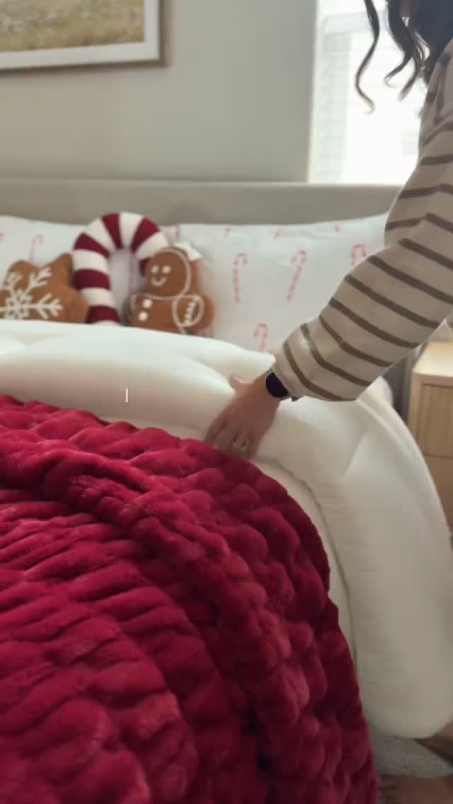 Red plush holiday blanket and Christmas pillows on a white bed.