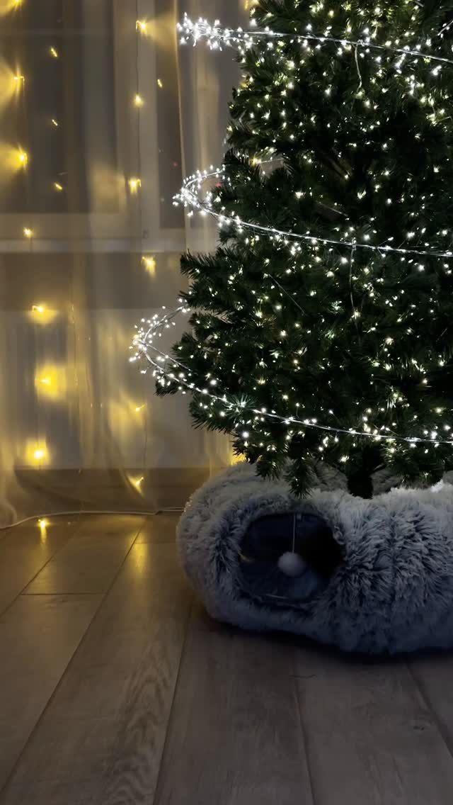 Christmas tree with white lights and grey faux-fur skirt on wooden flooring