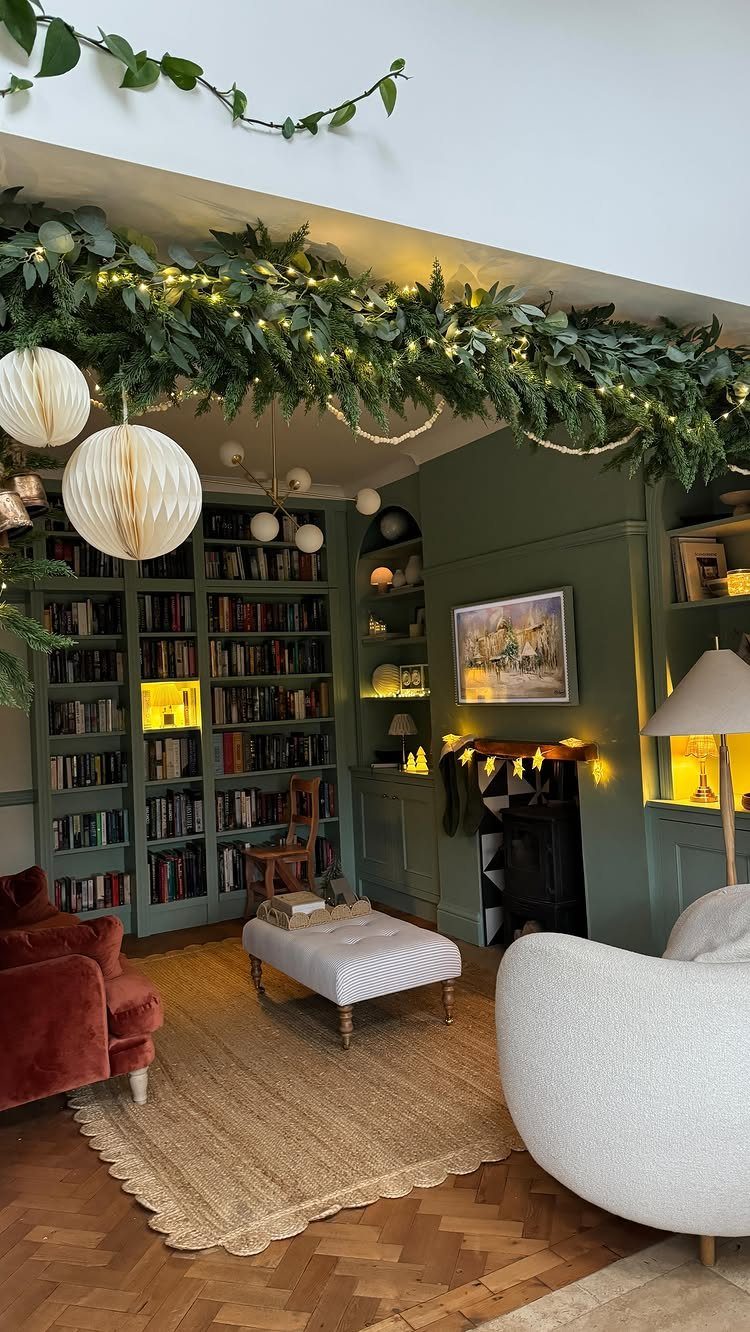 Living room with sage green walls, a large bookshelf, and festive ceiling garlands.