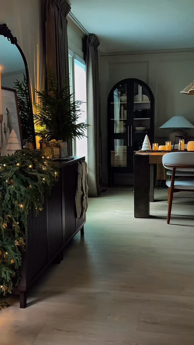 Dark wood console table with festive pine garland, fairy lights, and small tree.