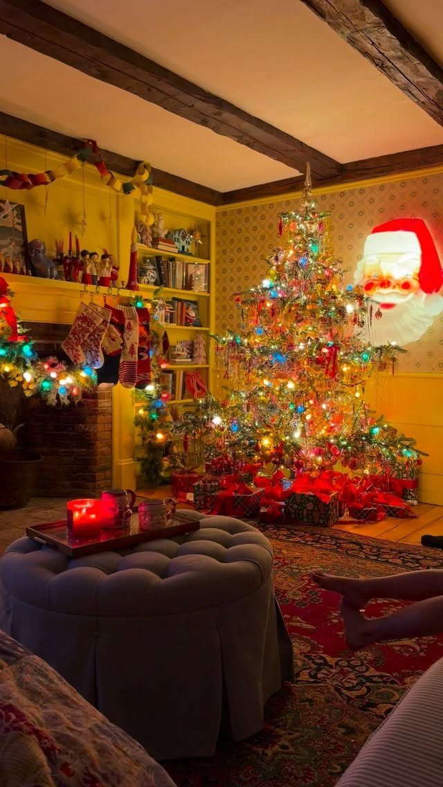 Two brightly lit Christmas trees in a yellow living room with a fireplace.