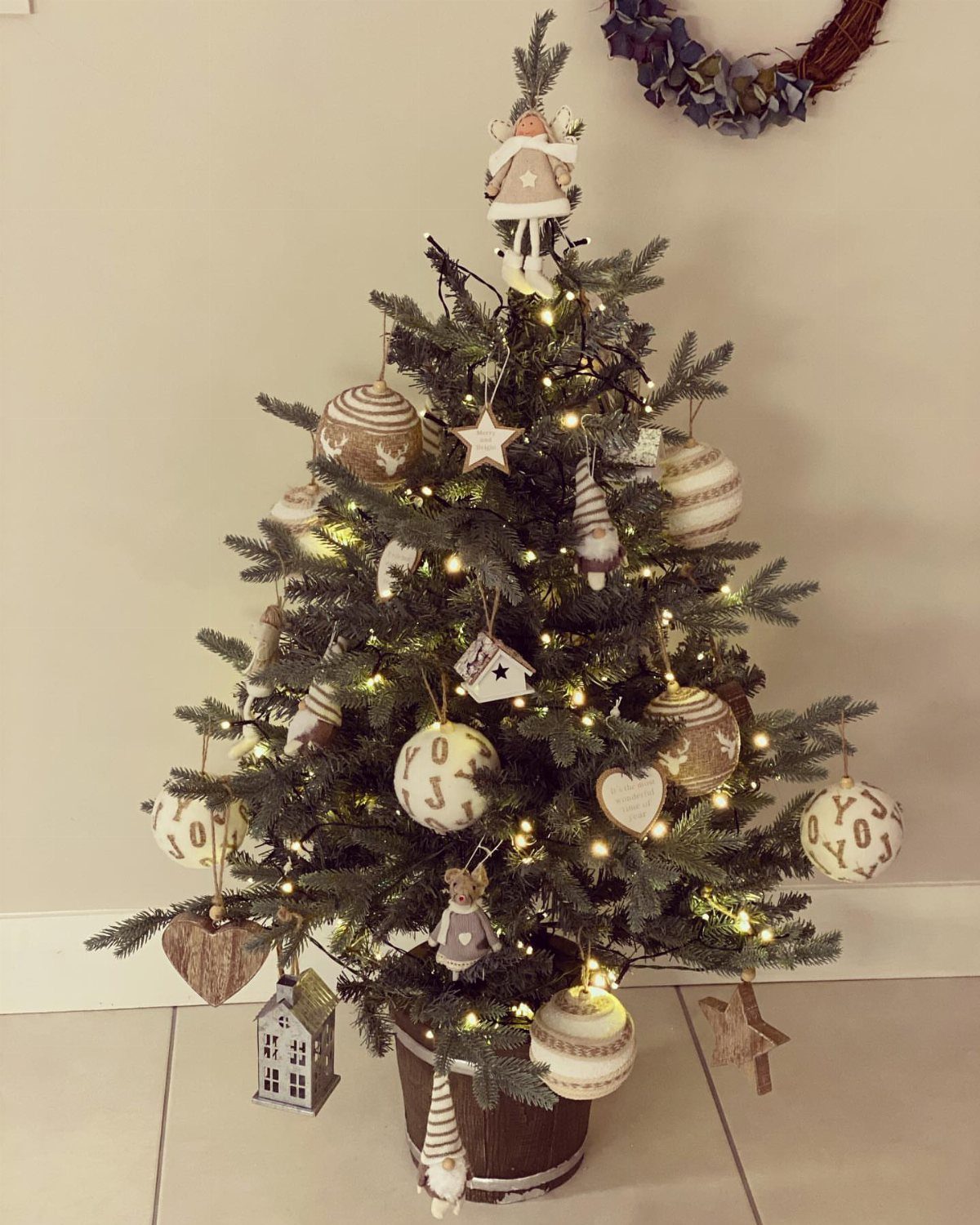 Decorated Christmas tree with neutral ornaments and warm lights in a brown pot.