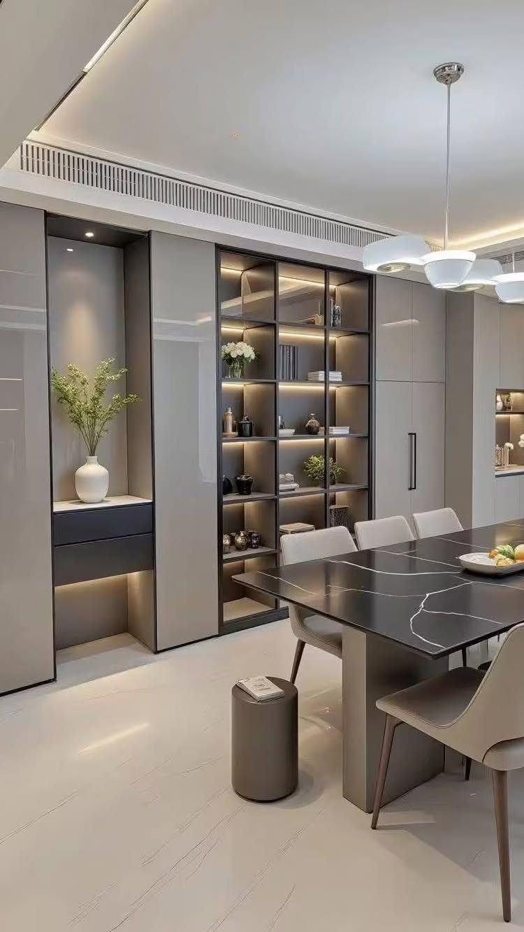 Modern dining room with black marble table, beige chairs, and illuminated built-in shelving.