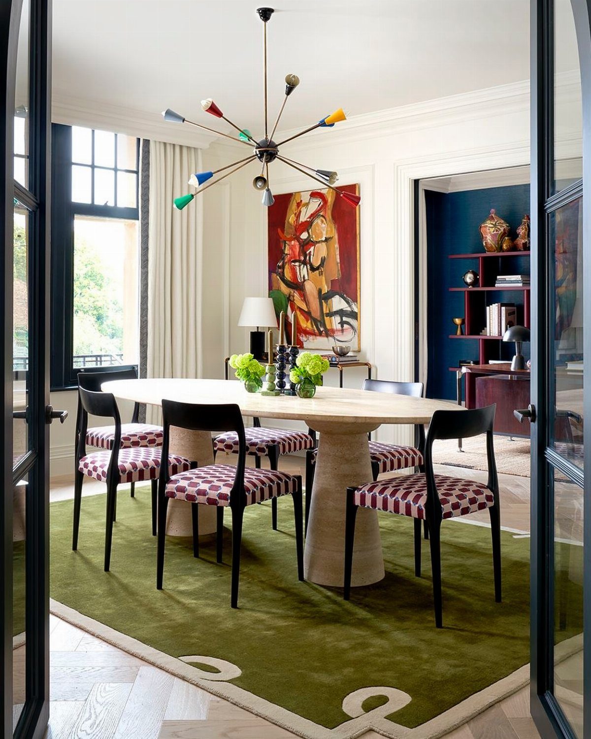 Round dining table with red patterned chairs on a green rug in a room.