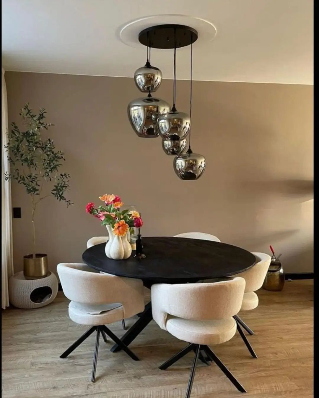Cluster of metallic spherical pendant lights hanging over a round black dining table.