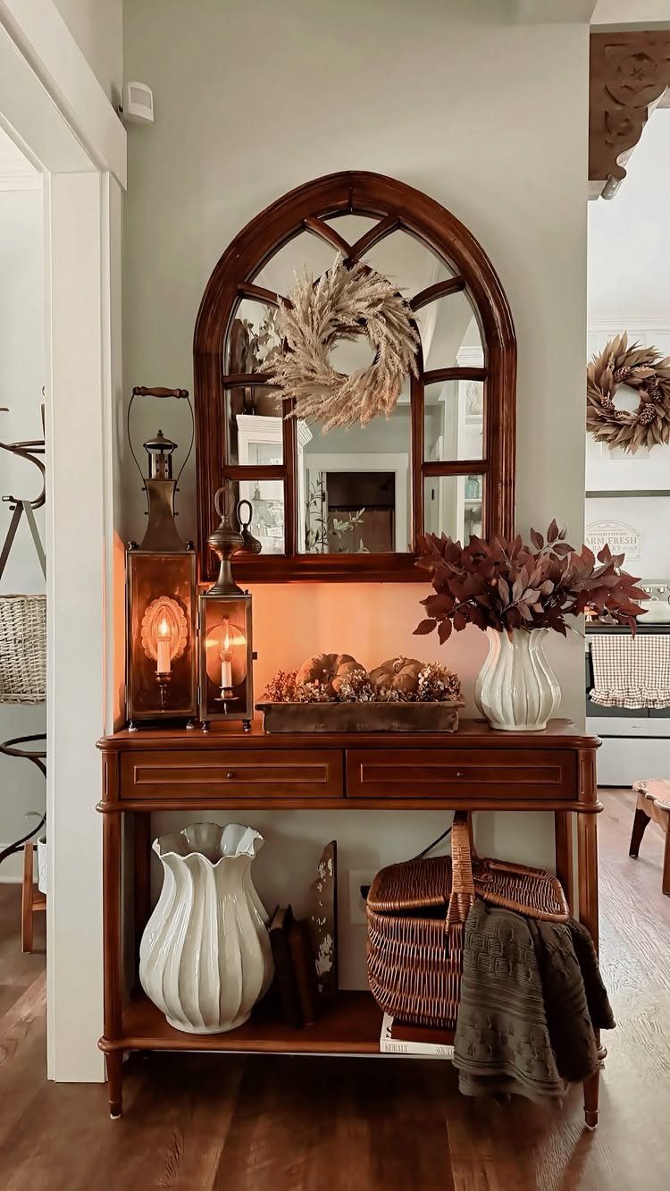 Wooden console table with an arched mirror, lanterns, and autumn decor against a wall.