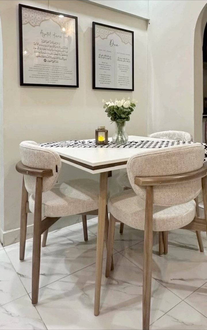 White square dining table with beige upholstered chairs and white flowers in vase.