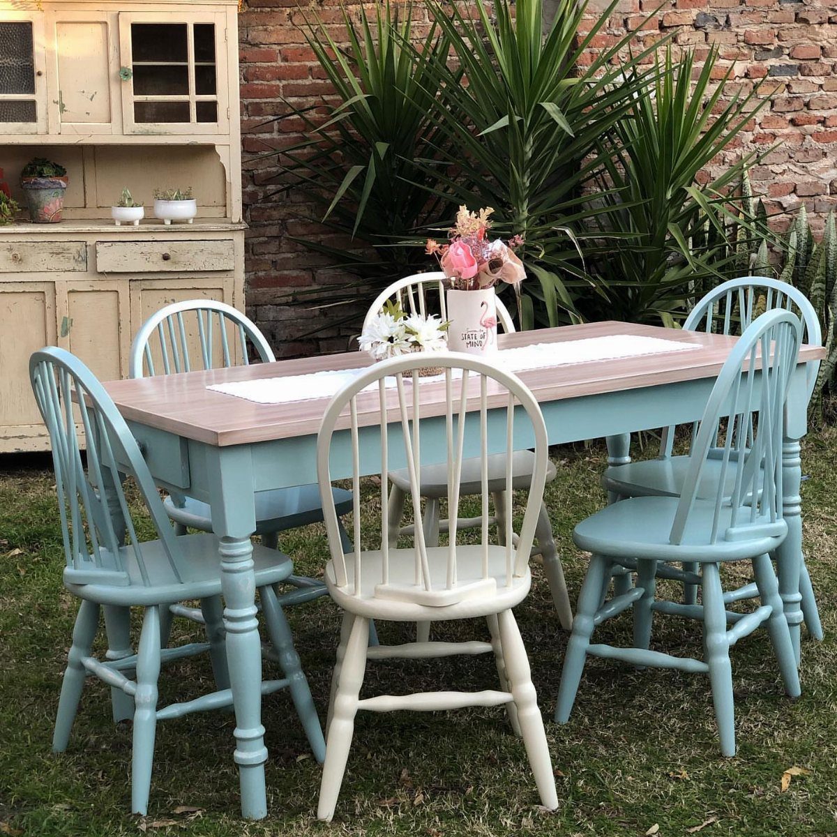 Light blue dining table with mismatched blue and cream spindle-back chairs outdoors.