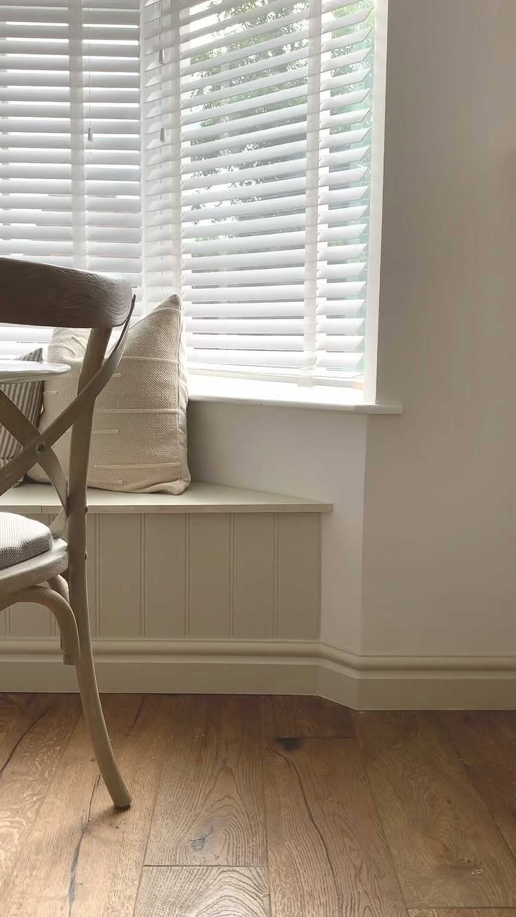 Built-in window seat with white paneling and a beige pillow in a bright room.