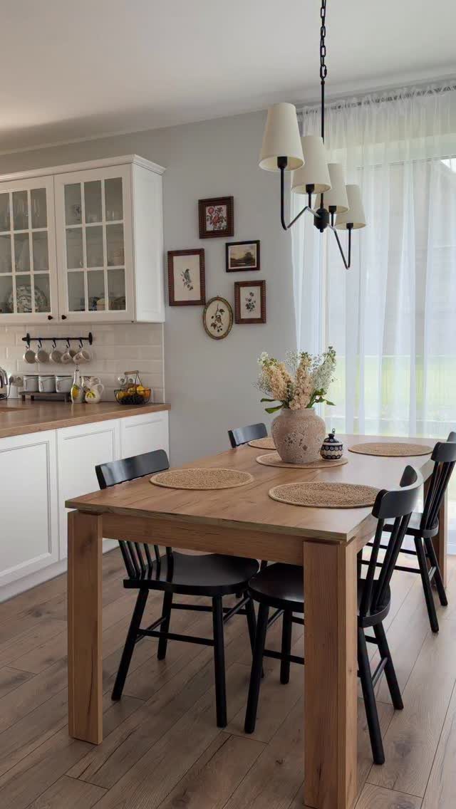 Light wood dining table with black chairs in a bright, airy farmhouse room.