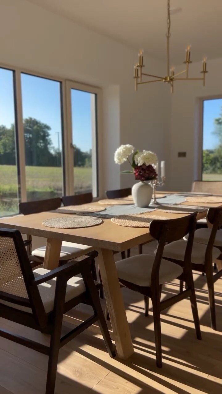 Wooden dining table with mismatched dark wood chairs and a gold chandelier.