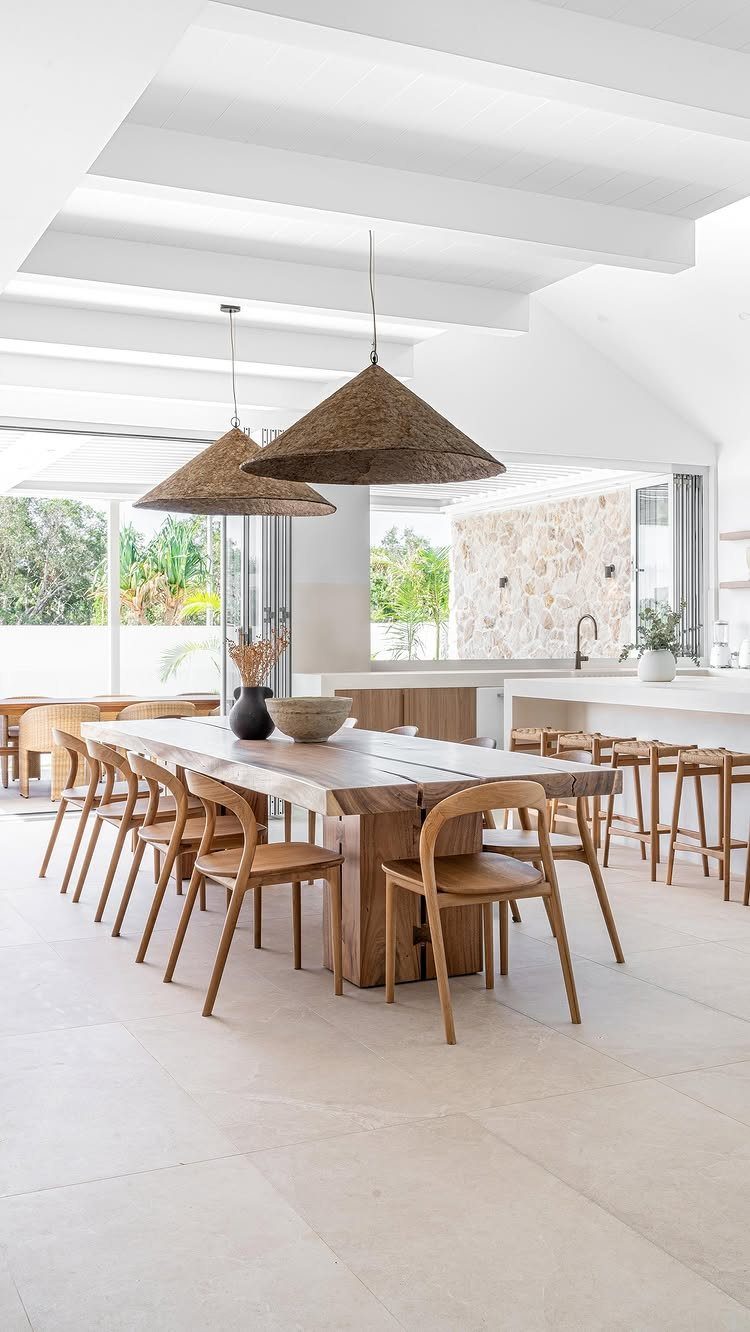 Large wooden dining table with matching chairs under woven conical pendant lights.