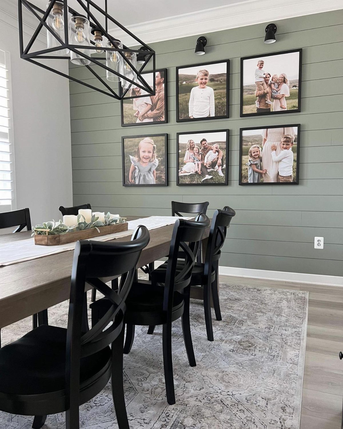 Sage green shiplap wall with family photos behind a wooden dining table.