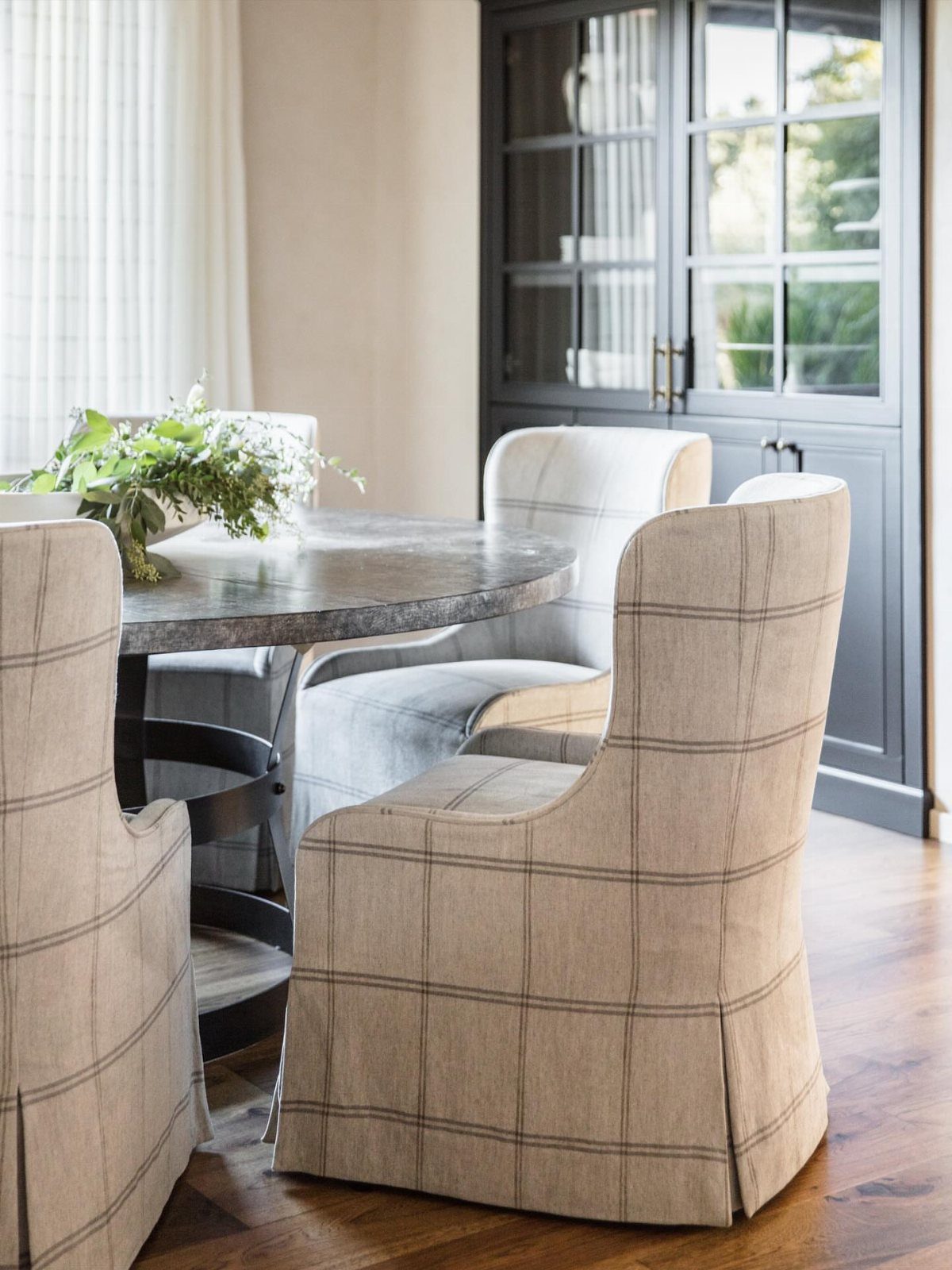 Plaid slipcovered dining chairs surrounding a round marble table in a bright room.