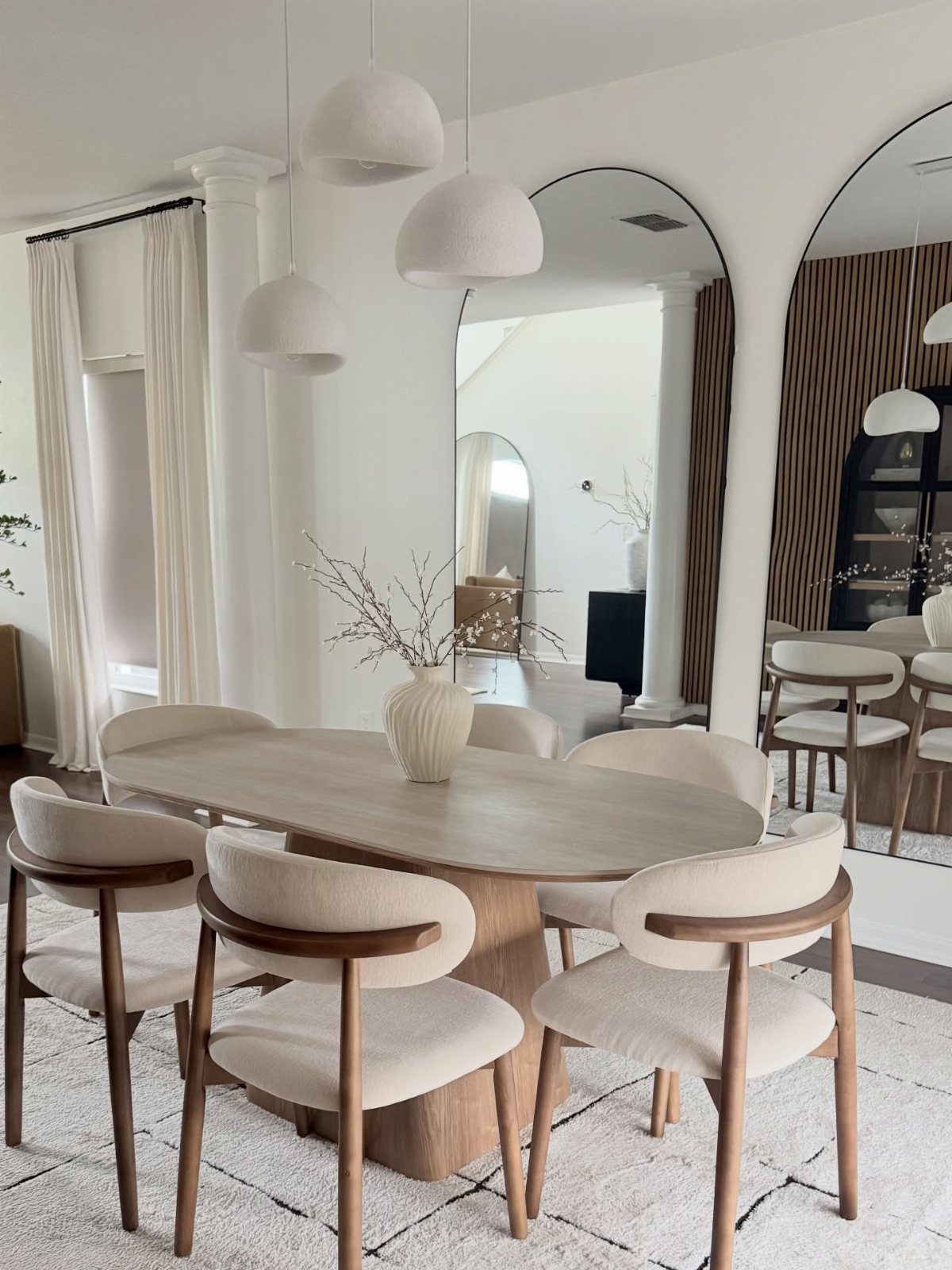 Oval wooden dining table with matching upholstered chairs in a bright white room