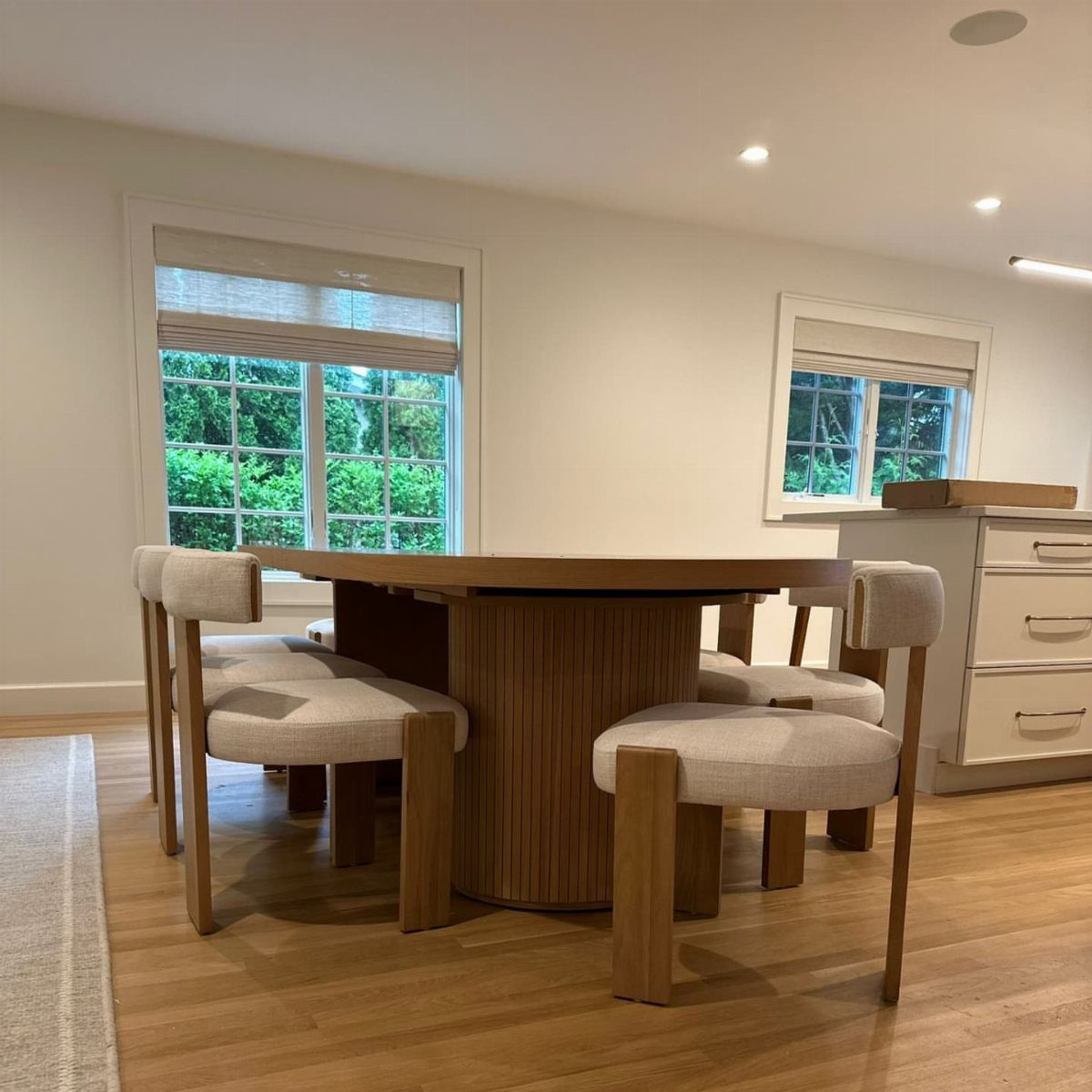 Round wooden dining table with fluted base and matching upholstered chairs in bright room