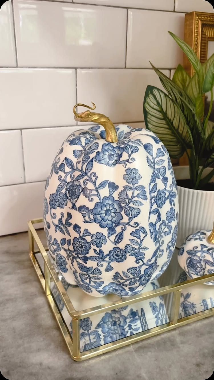 Navy blue floral ceramic pumpkin on a gold mirrored tray with white tiles.